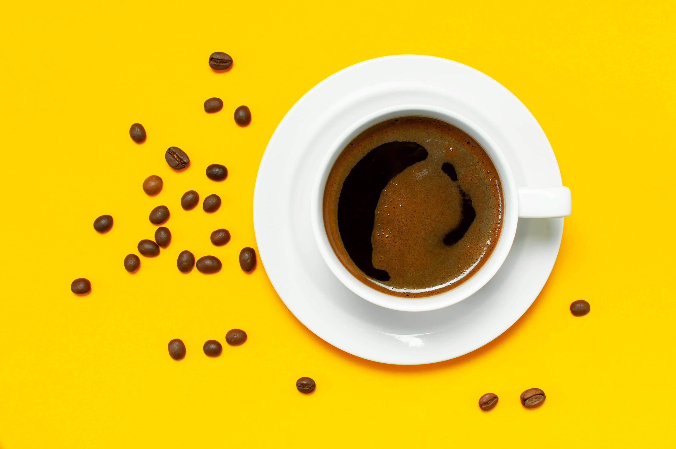 Tasse de café blanche sur un fond jaune avec des grains de café