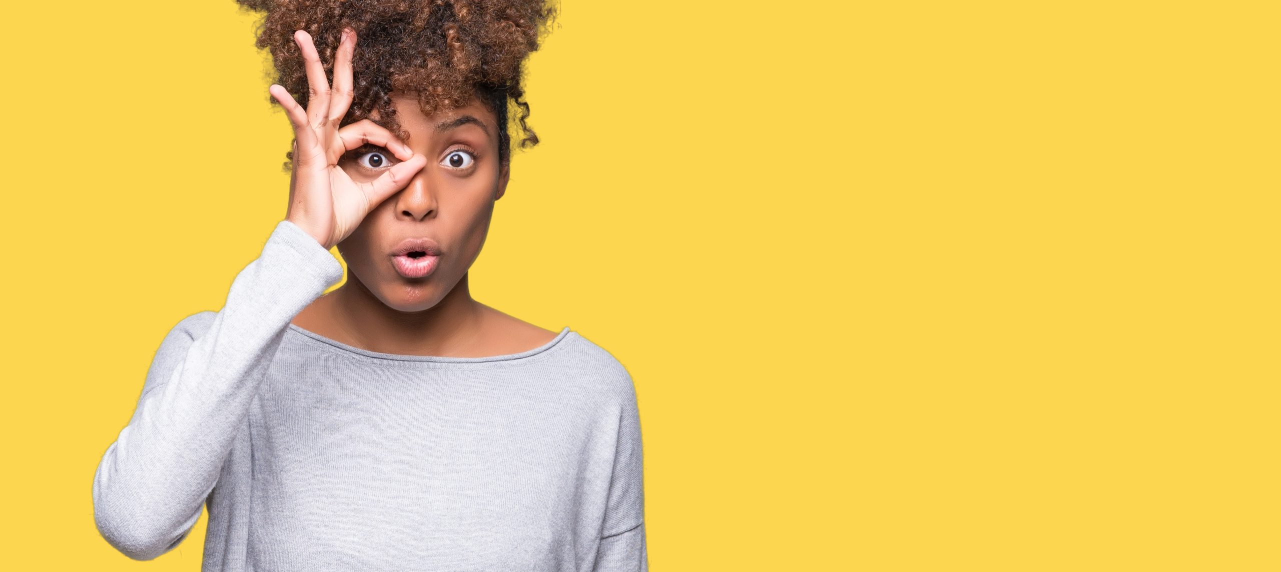 Beautiful young african american woman over isolated background doing ok gesture shocked with surprised face, eye looking through fingers. Unbelieving expression.