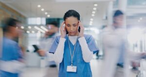 Une femme soignante à l'hôpital, qui est entourée de ses collègues, qui sont floutés autour d'elle.